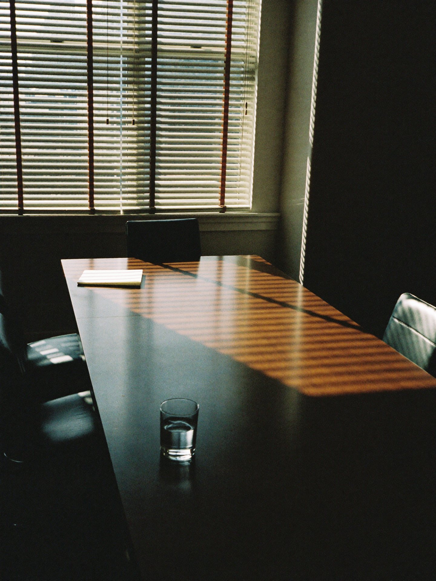 An empty meeting room before a difficult conversation: one chair pulled out, morning light through the blinds