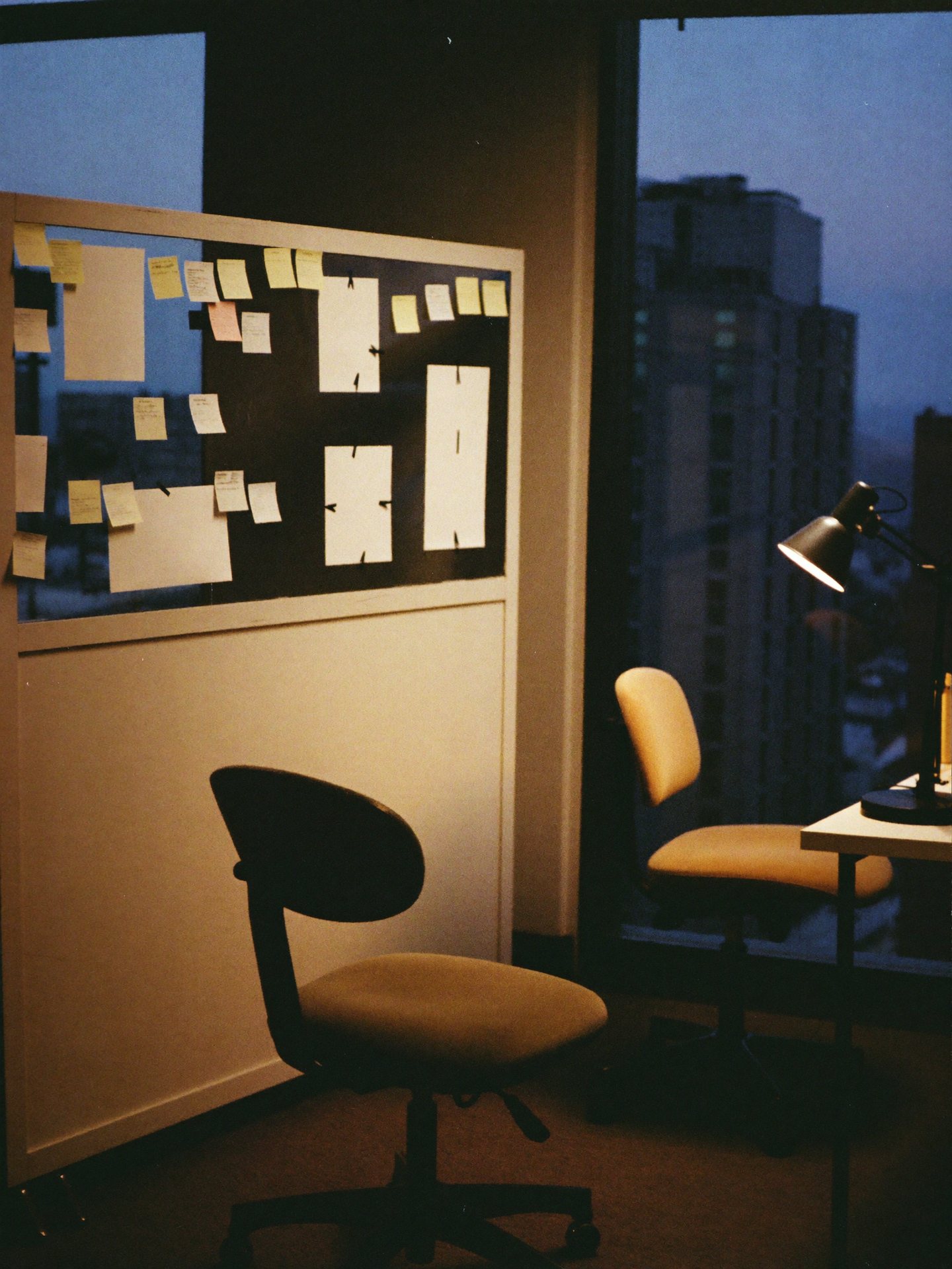 A founder’s office after hours: an empty chair and a planning wall of notes against the dusk